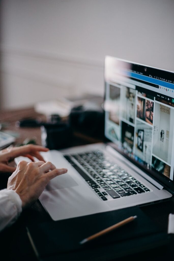 Close-up of hands typing on a laptop keyboard displaying a photo gallery webpage