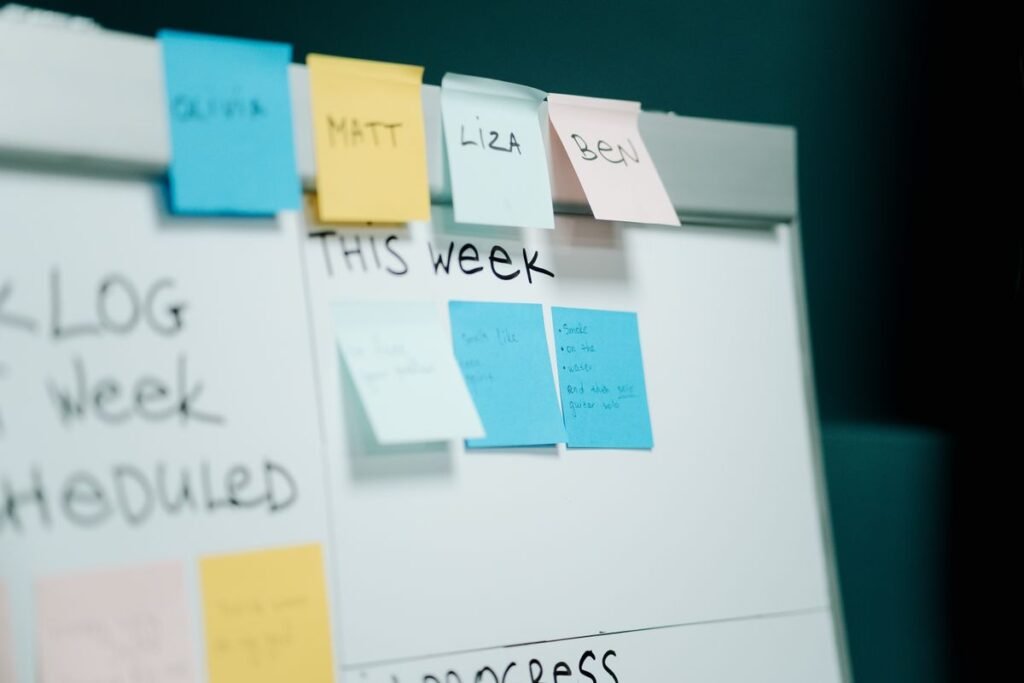 A whiteboard with colour-coded sticky notes labelled with names under a This Week heading, representing a content planning workflow